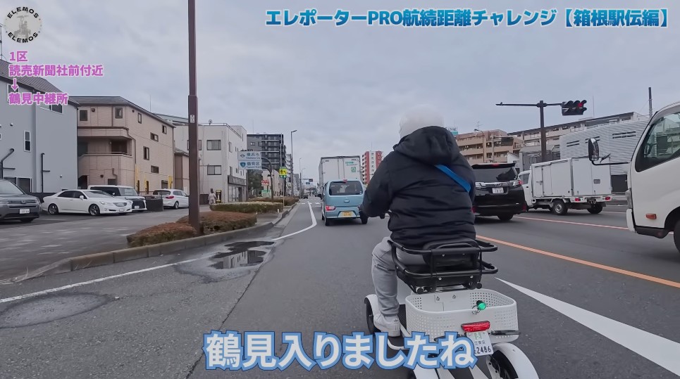 2026-05-04_163543 | ELEMOs Person on a mobility scooter riding in a busy Japanese city street, seen from behind, with cars and buildings around.