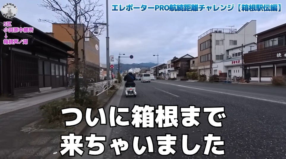 2026-05-04_175350 | ELEMOs Street view in a Japanese town with a person on a scooter driving ahead; large on-screen caption in Japanese reads 'ついに箱根まで来ちゃいました' (Finally arrived in Hakone).