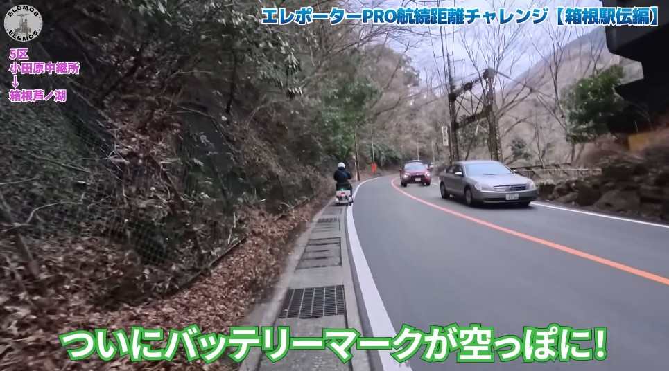 2026-05-04_181428 | ELEMOs Cyclist riding on the roadside of a winding mountain road as cars pass; green caption reads 'Battery mark is finally empty!'