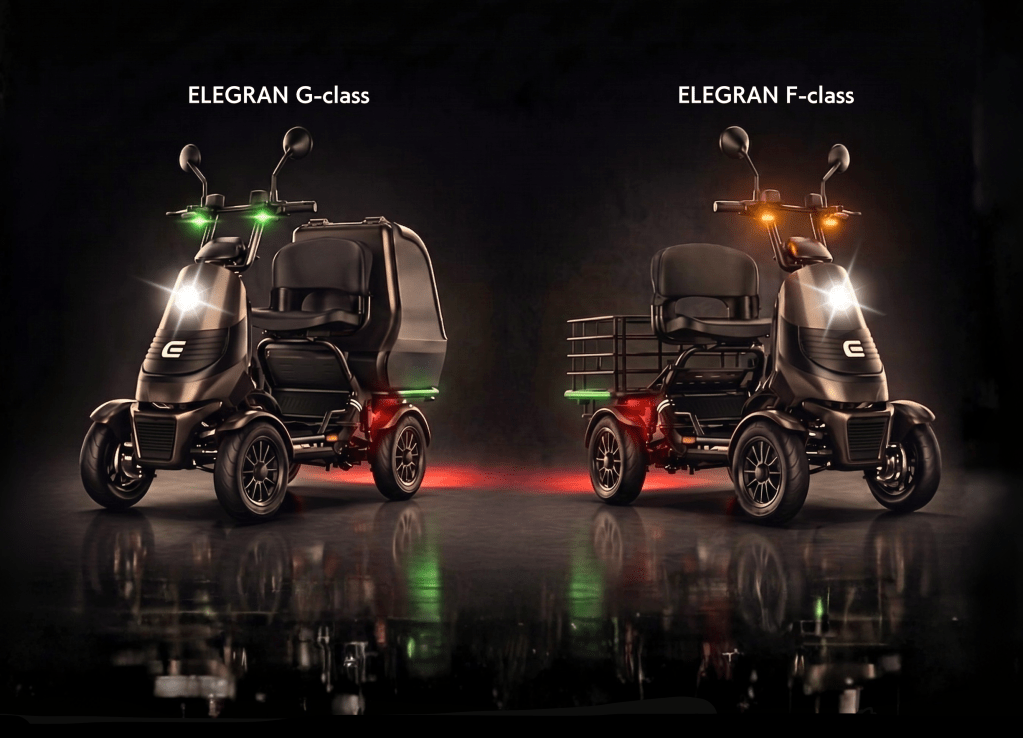 Two dark electric scooters side by side in a dim studio, with green front lights on the left and orange accents on the right, labeled G-class and F-class above each.