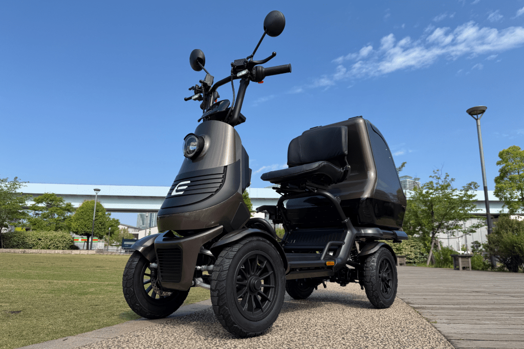 Close-up of a matte brown electric scooter, showing the handlebars, mirrors, and front headlight against a clear blue sky.