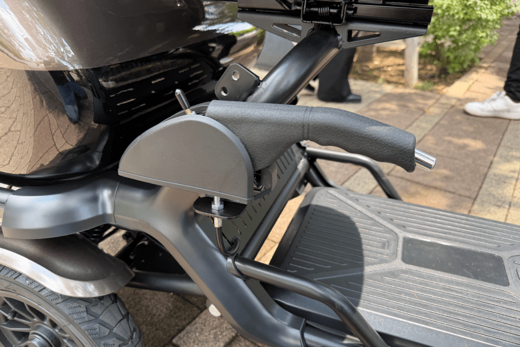 Close-up of a motorcycle/scooter frame showing the textured right handle grip and rear step area with a metal bracket and bolt nearby.