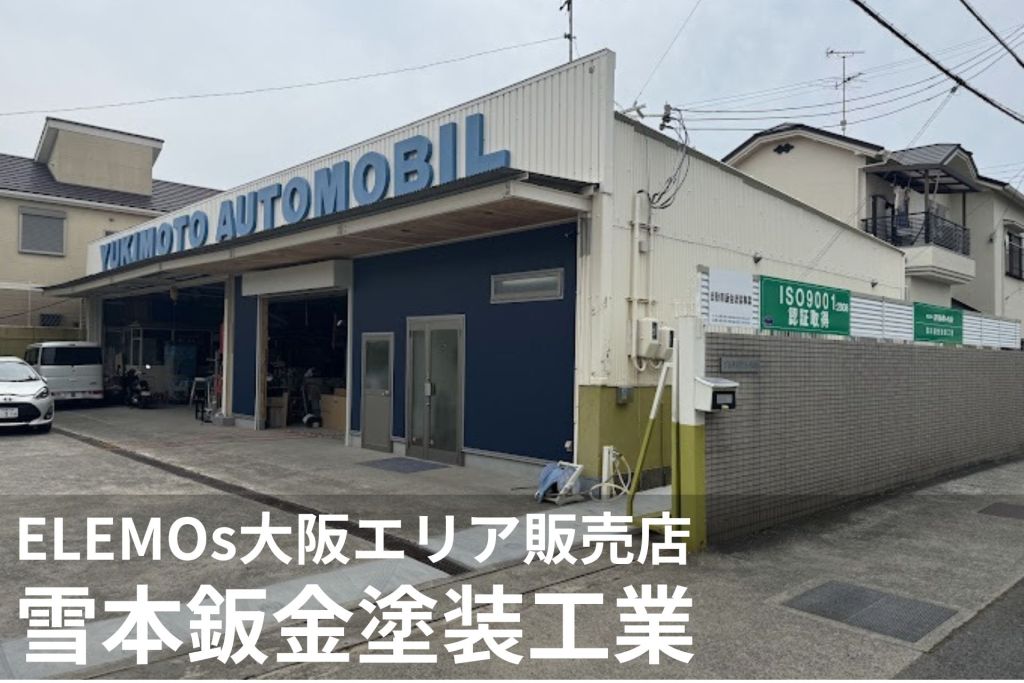 Auto repair shop with a blue front and a large sign reading 'YUKIMOTO AUTOMOBILES' above the bay; a white van is parked outside.