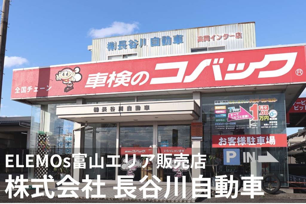Exterior of a Japanese auto service center with a large red sign reading '車検のコバック' and a cartoon mascot, storefront with glass doors and parking area under a blue sky.