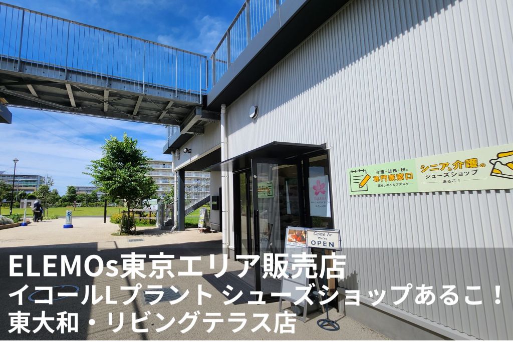 Exterior view of a modern white building with a metal walkway above, blue sky, and green trees beside a storefront with an OPEN sign.