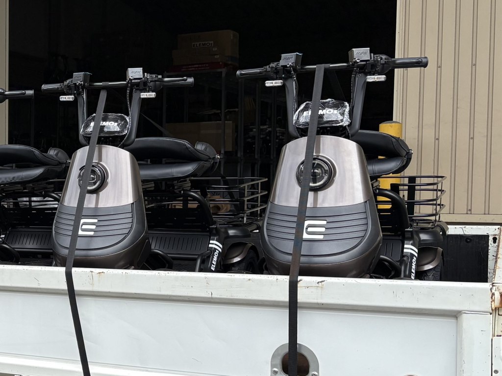 Two gray ELEMOS electric scooters strapped for transport in a truck bed or trailer.