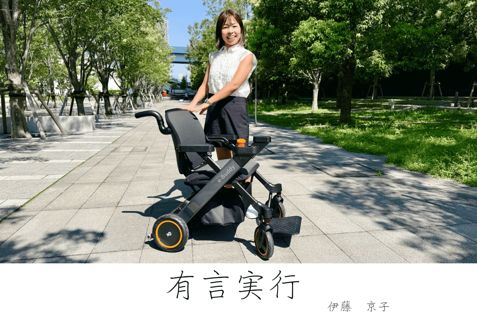 Smiling woman in a white blouse pushes a black e-Buddy mobility scooter along a sunny tree-lined park path.