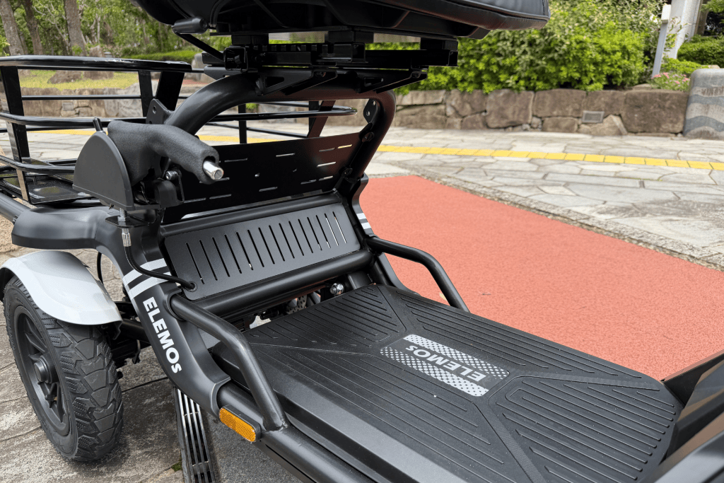 Electric wheelchair parked outdoors, showing the footplate, frame, and rear wheel.