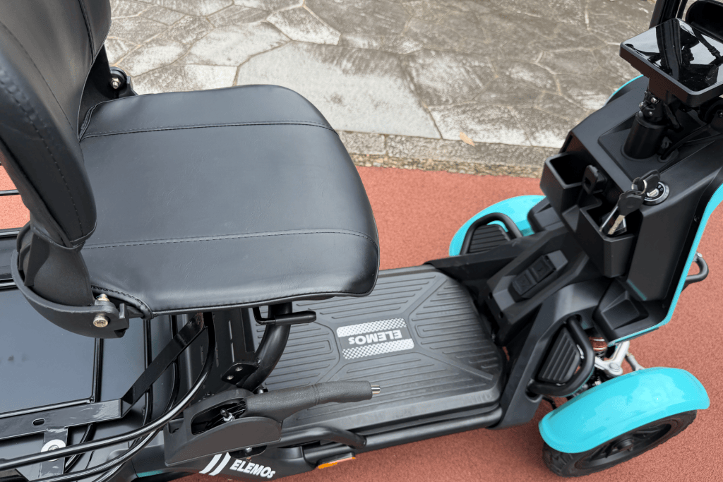 Close-up of a black scooter seat and footboard with turquoise fenders and ignition key inserted on the right side of the handlebar area, Eleos branding visible.