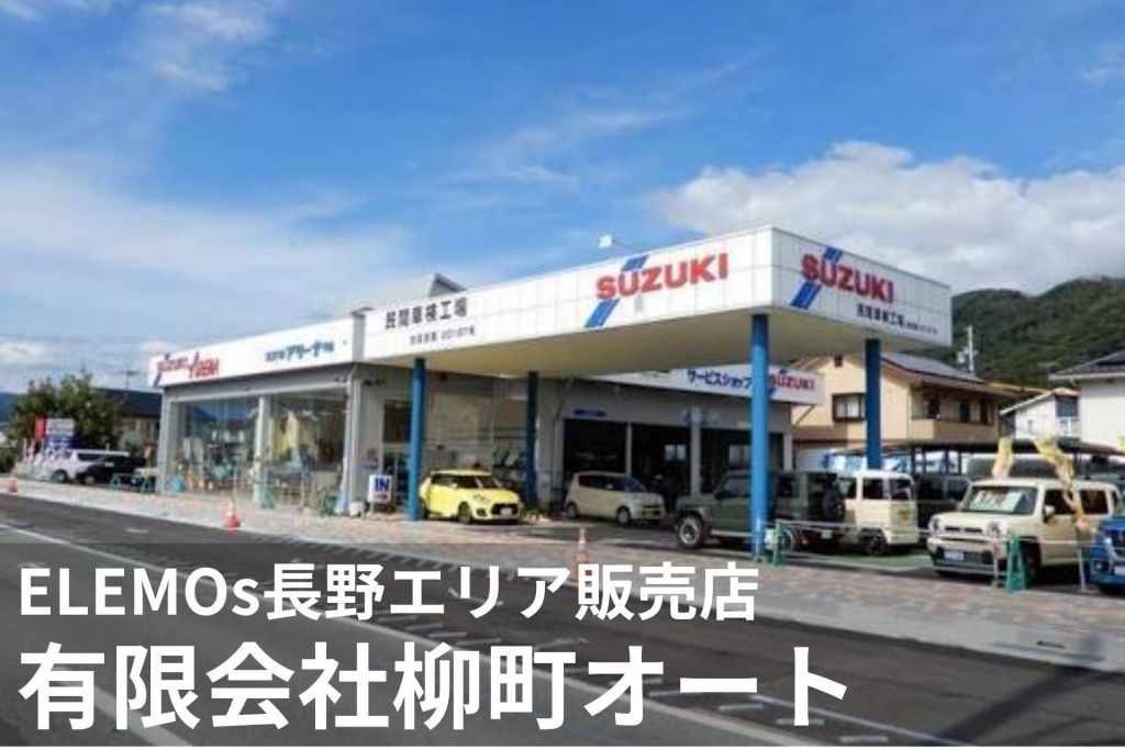 Suzuki car dealership in Japan with showroom and service bays, blue support columns, and several cars parked outside against a blue sky.